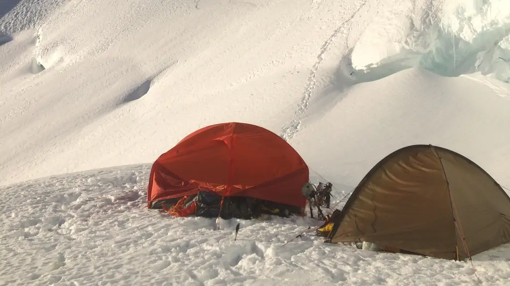 Two tents pitched on a glacier, a boot track climbing the snow slope behind them