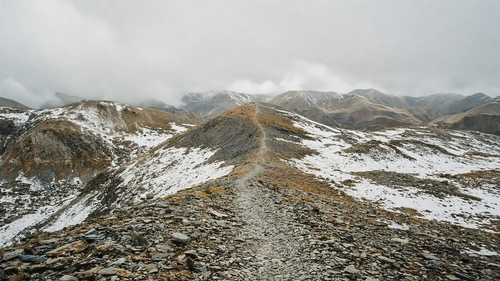 Rocky ridge trail with patches of fresh snow under low cloud